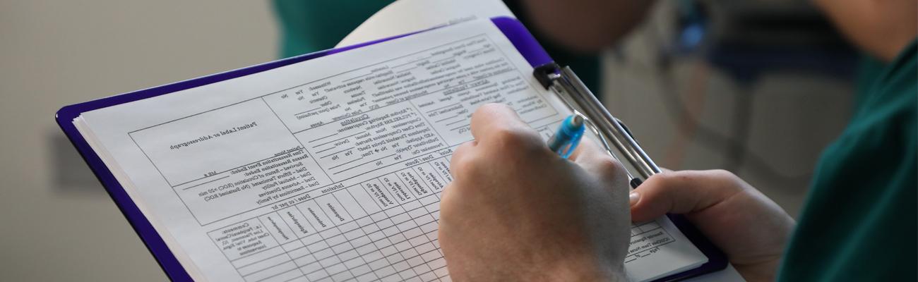 Nursing simulation student writing notes on a clipboard