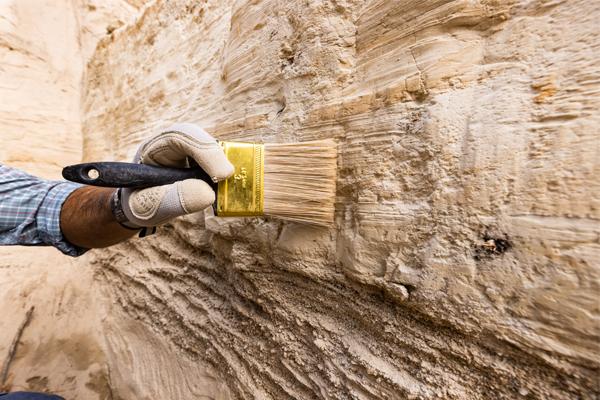 Hand using a brush on a dirt wall