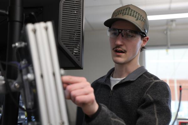 Man wearing safety glasses pointing at a computer monitor